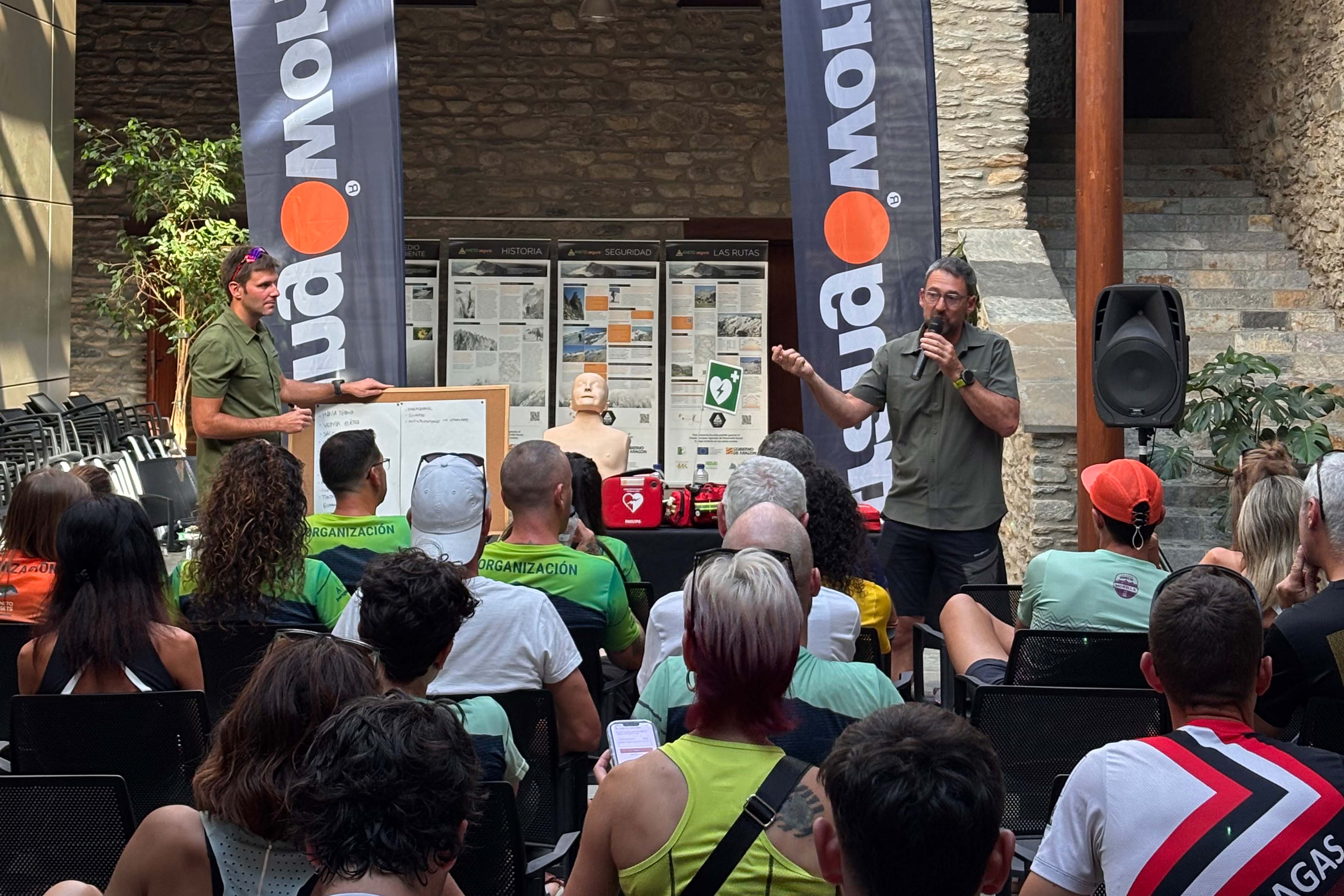 Charla de seguridad en montaña con banderolas Trangoworld Ponente explicando técnicas de RCP ante público en una charla de seguridad