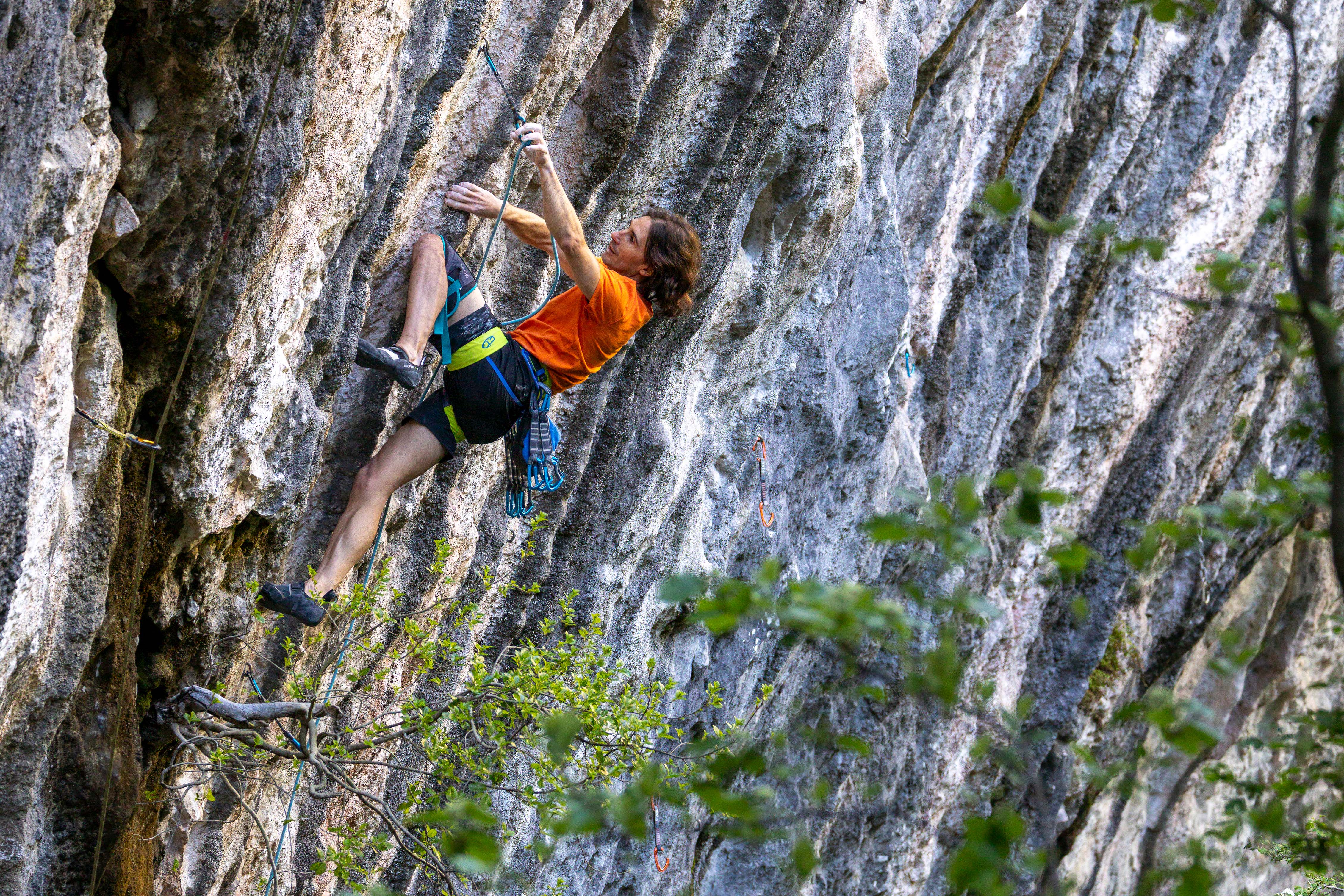 Escalador subiendo una pared de roca caliza vertical Escalador con camiseta naranja trepando una pared de roca caliza