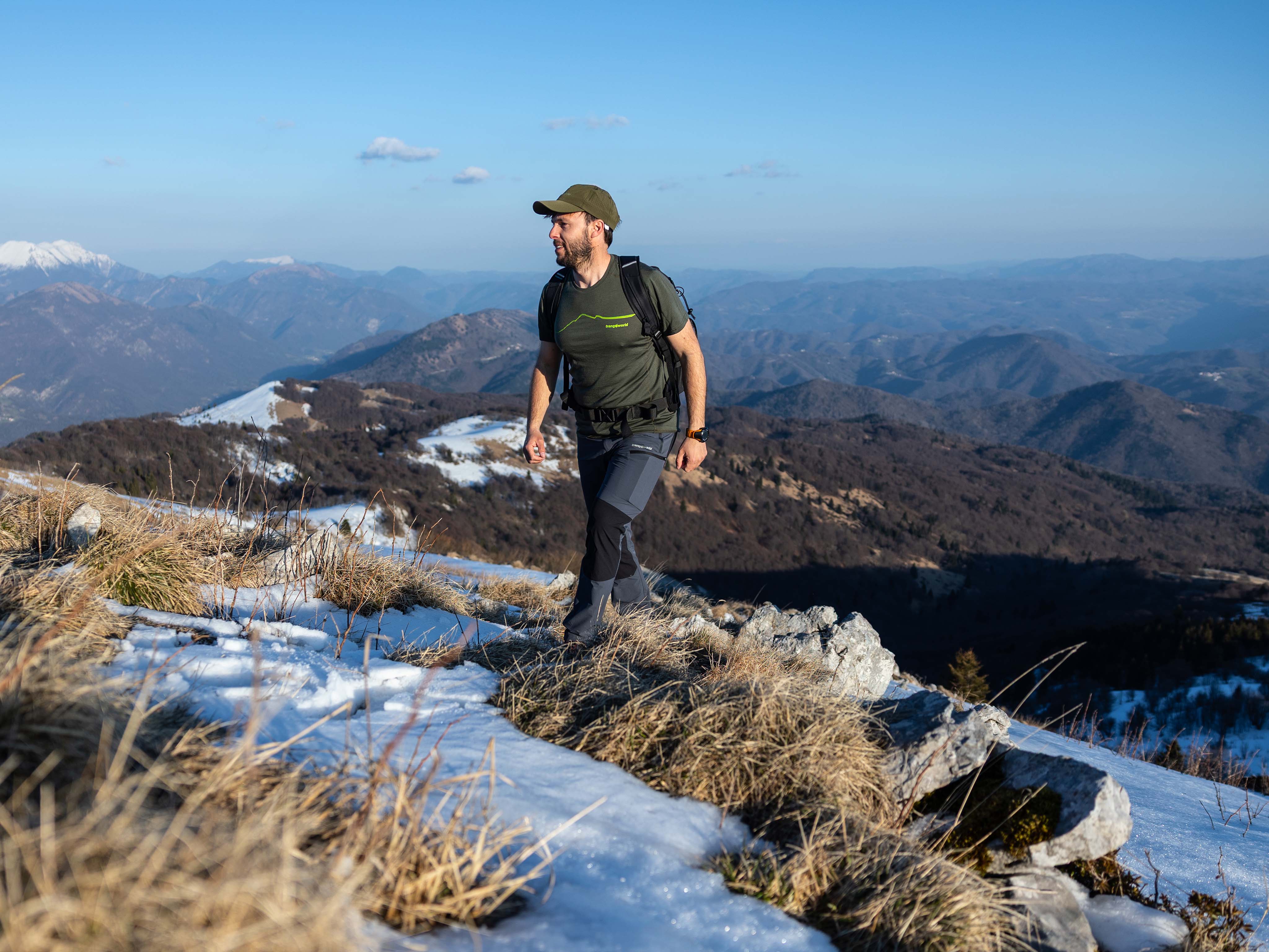 Senderista caminando por una cresta cubierta de nieve Hombre con camiseta de lana merino Trangoworld verde caminando en cresta de montaña con nieve
