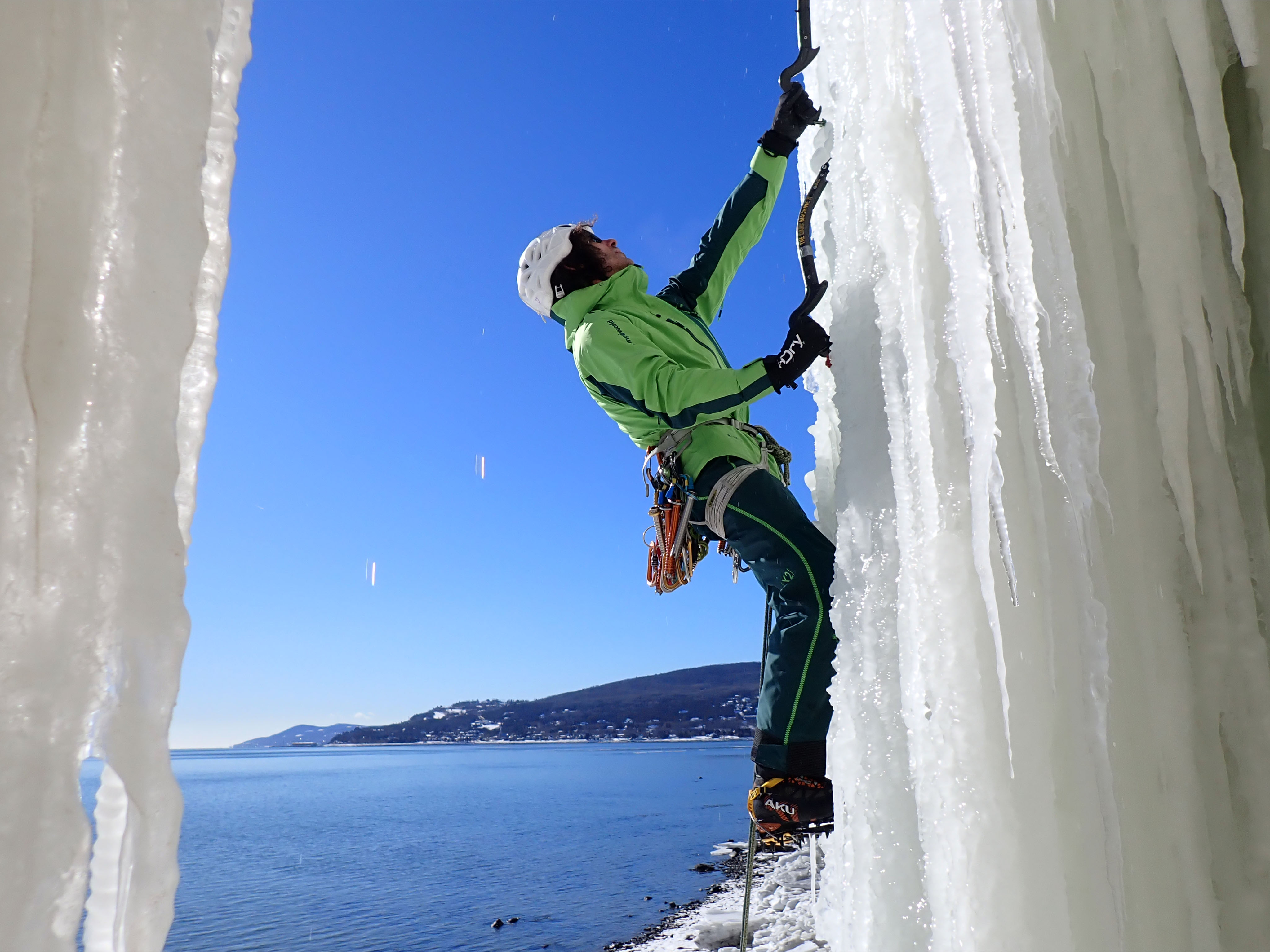Santi Padr&oacute;s escalando en una cascada de hielo con equipamiento t&eacute;cnico Trangoworld y mar azul al fondo
