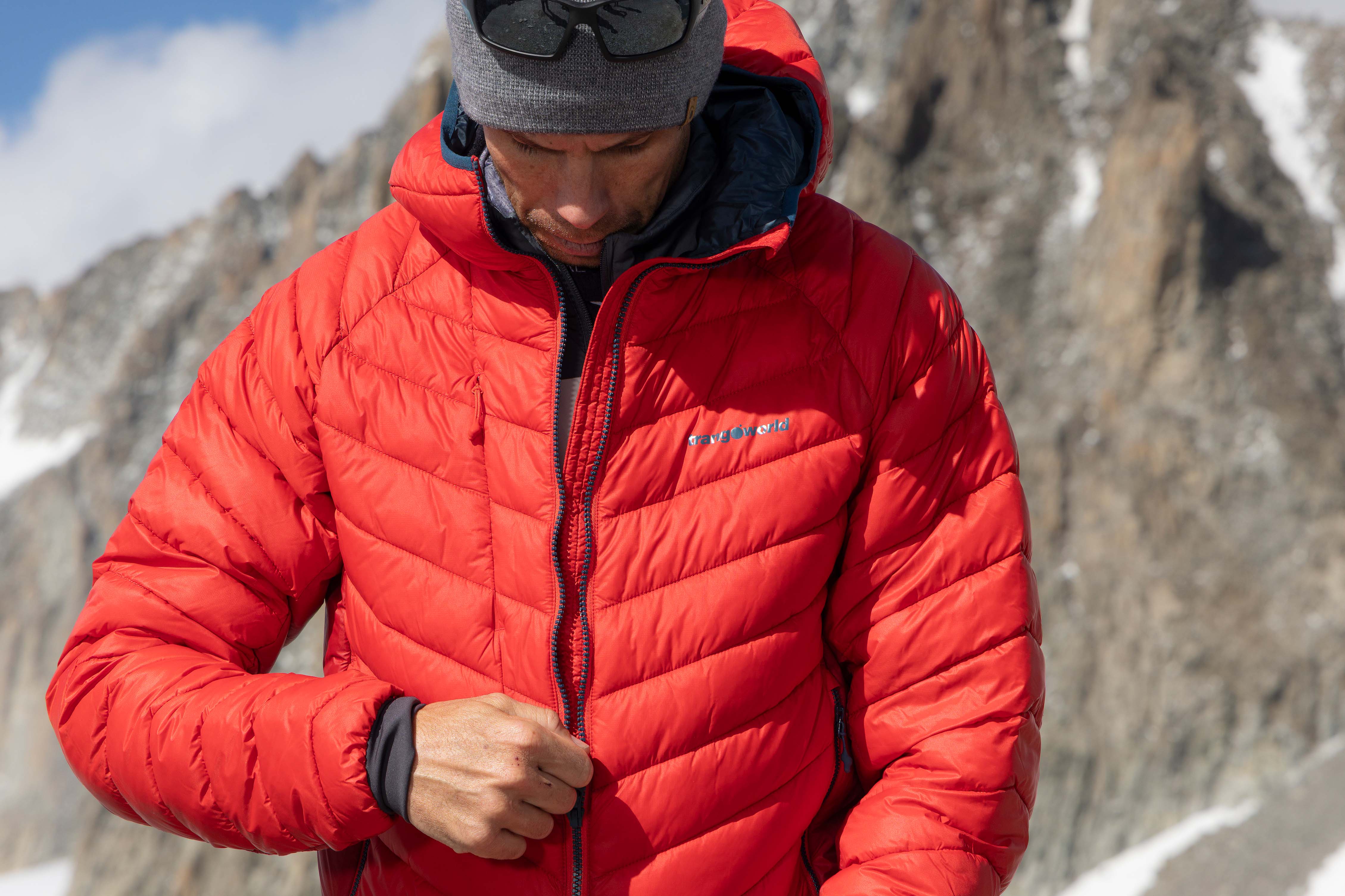 Sistema de capas en montaña. Segunda capa. Trangoworld Hombre con chaqueta de fibra roja Trangoworld como segunda capa en montaña con pared rocosa de fondo