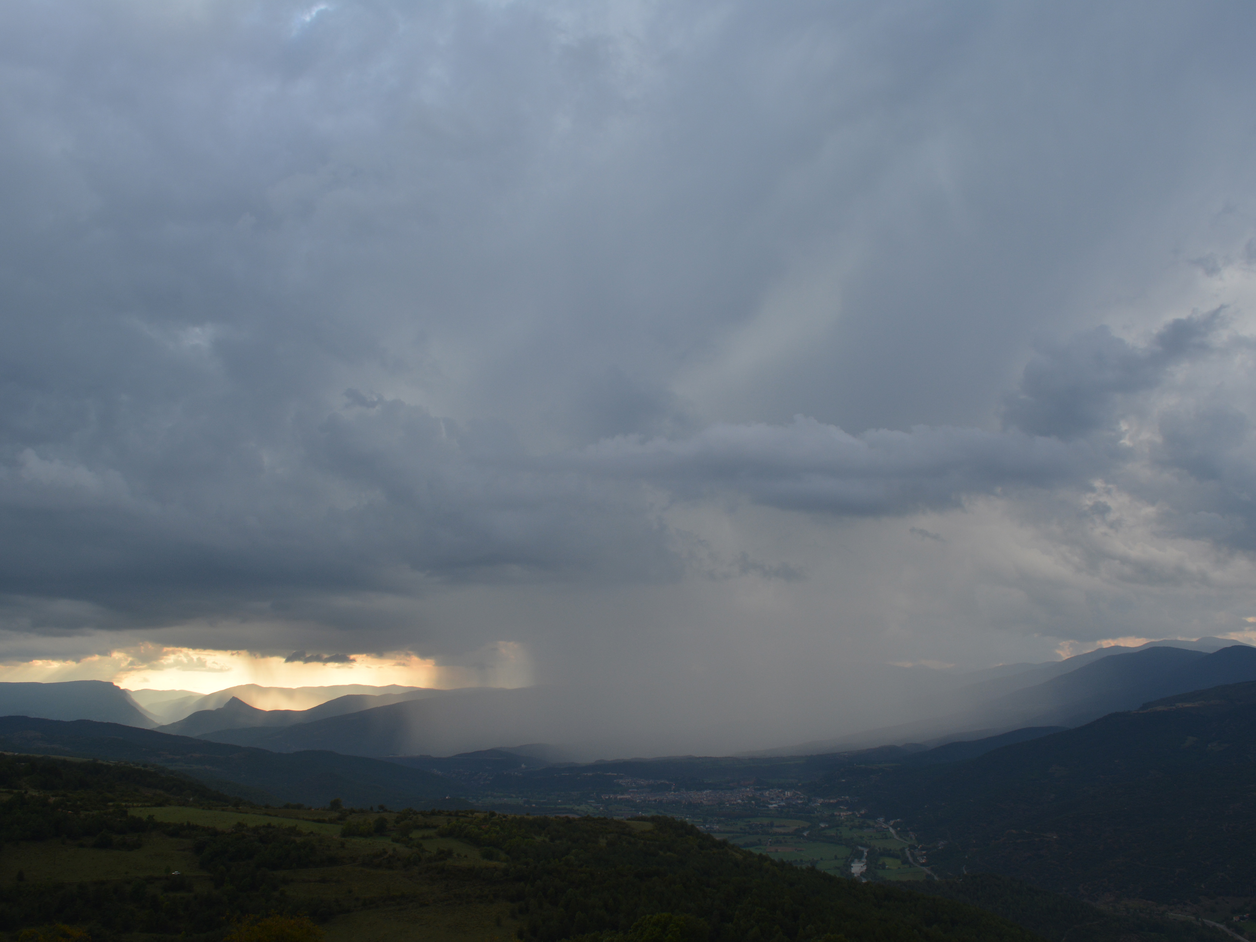 Tormenta descargando lluvia sobre un valle de montaña Cortina de lluvia cayendo sobre un valle de montaña al atardecer